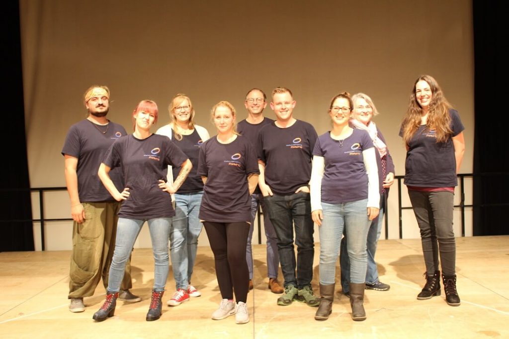 3 Männer und 6 Frauen in blauen T-Shirts, die in einer Gruppe stehen